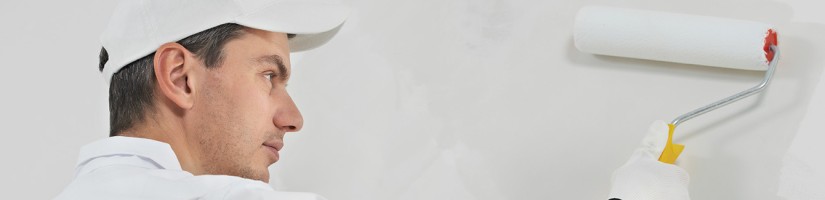 Ein Maler streicht mit einer Farbrolle eine Wand weiß an.