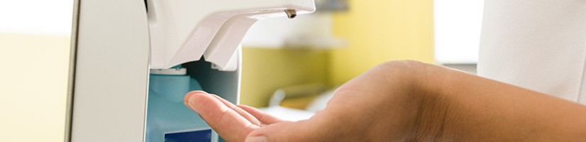 Ein Mensch betätigt den Hebel eines Desinfektionsgerätes, um sich die Hände zu desinfizieren.