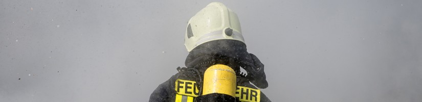 Eine Feuerwehreinsatzkraft mit Atemschutz steht im dichten Rauch.