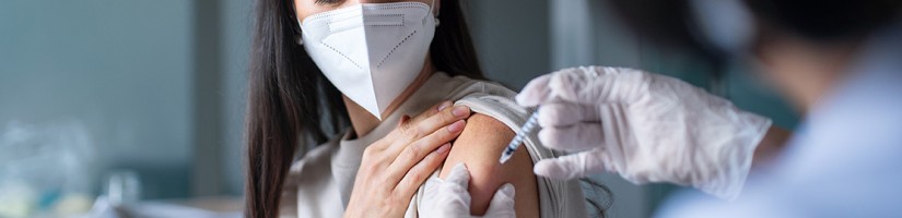 Eine Frau trägt eine Maske und wird in den Oberarm geimpft.