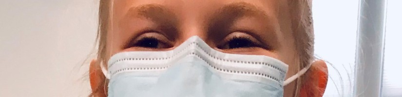Ein Mädchen mit einer OP-Maske schaut in die Kamera.