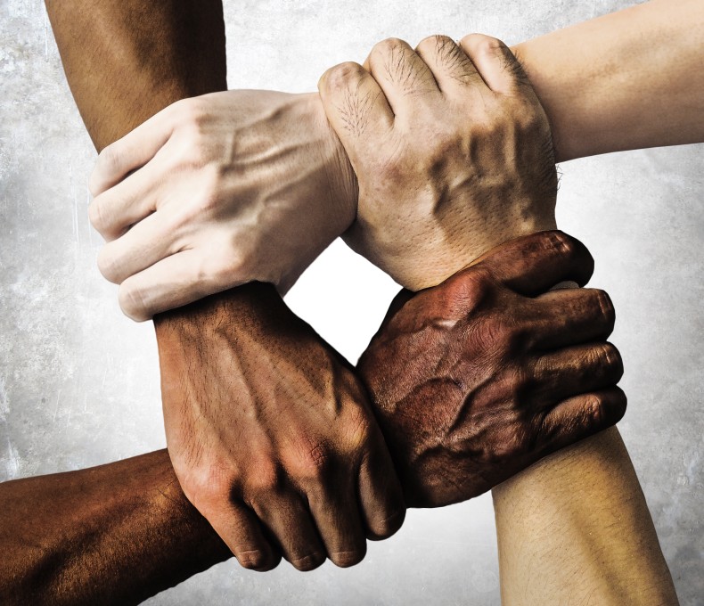 Vier Hände mit unterschiedlicher Hautfarbe greifen ineinander.