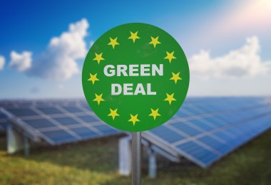 Auf einem grünen runden Schild steht: Green Deal; im Hintergrund sind Solarpanele zu sehen