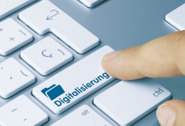 Eine Nahaufnahme einer Computertastatur mit einer speziellen Taste, auf der das Wort „Digitalisierung“ und ein Symbol eines Ordners abgebildet sind. Eine Fingerkuppe drückt die Taste, was den Prozess der digitalen Transformation symbolisiert.