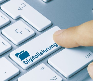 Eine Nahaufnahme einer Computertastatur mit einer speziellen Taste, auf der das Wort „Digitalisierung“ und ein Symbol eines Ordners abgebildet sind. Eine Fingerkuppe drückt die Taste, was den Prozess der digitalen Transformation symbolisiert.